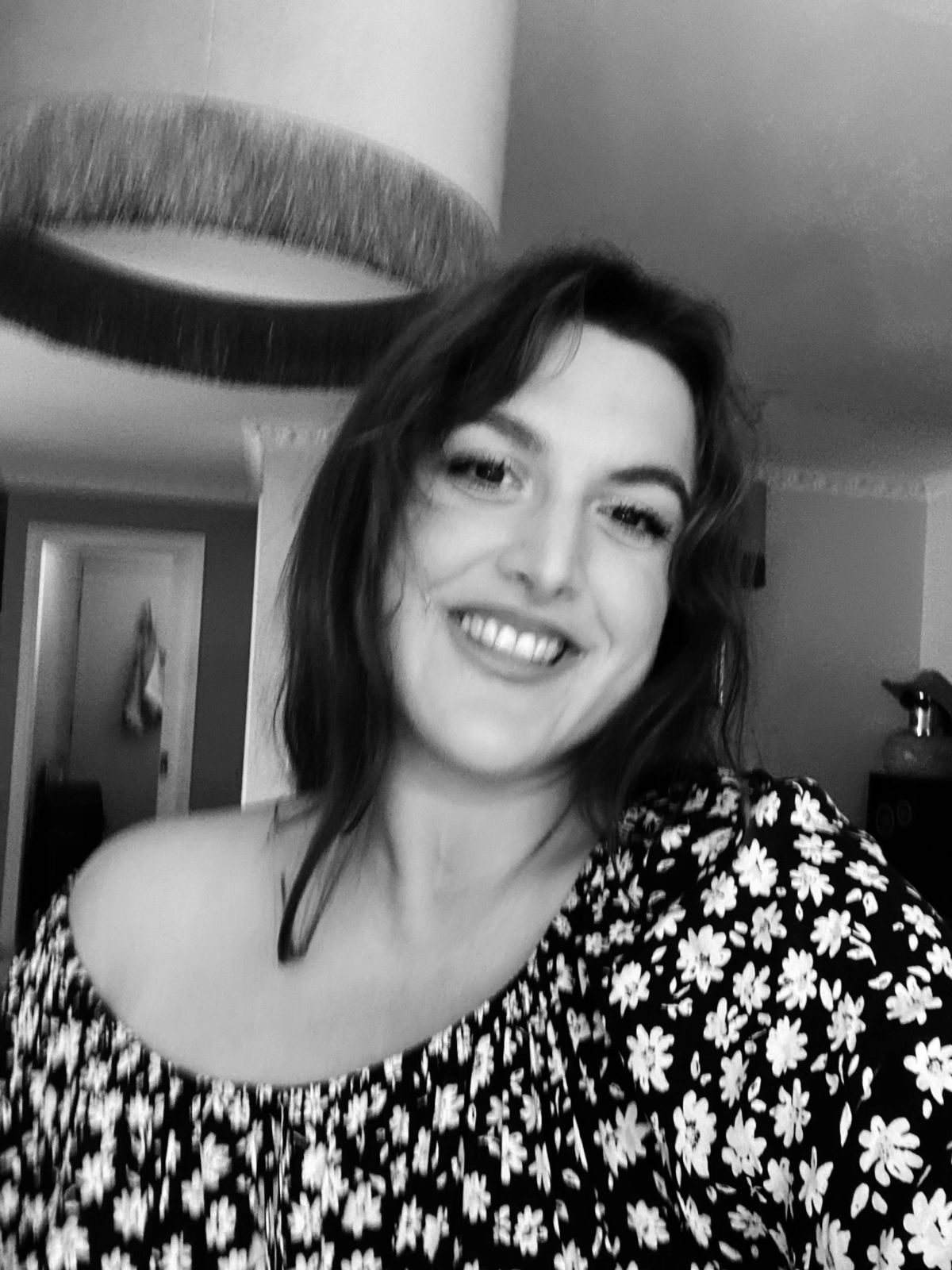Jess smiling with her head tilted, in a floral top, black and white