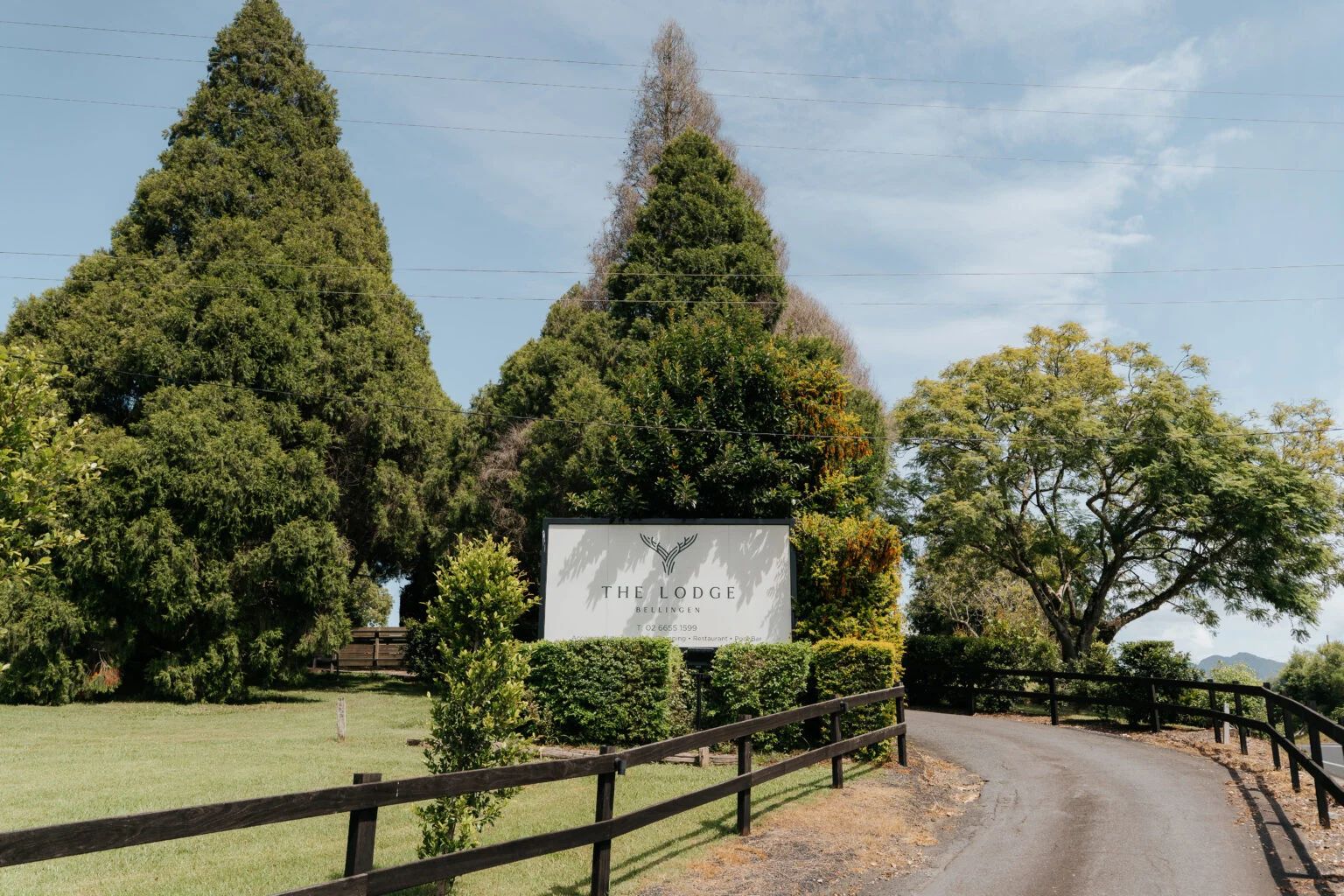 The Lodge Bellingen's sign at the driveway entrance, tall trees behind a timber fence